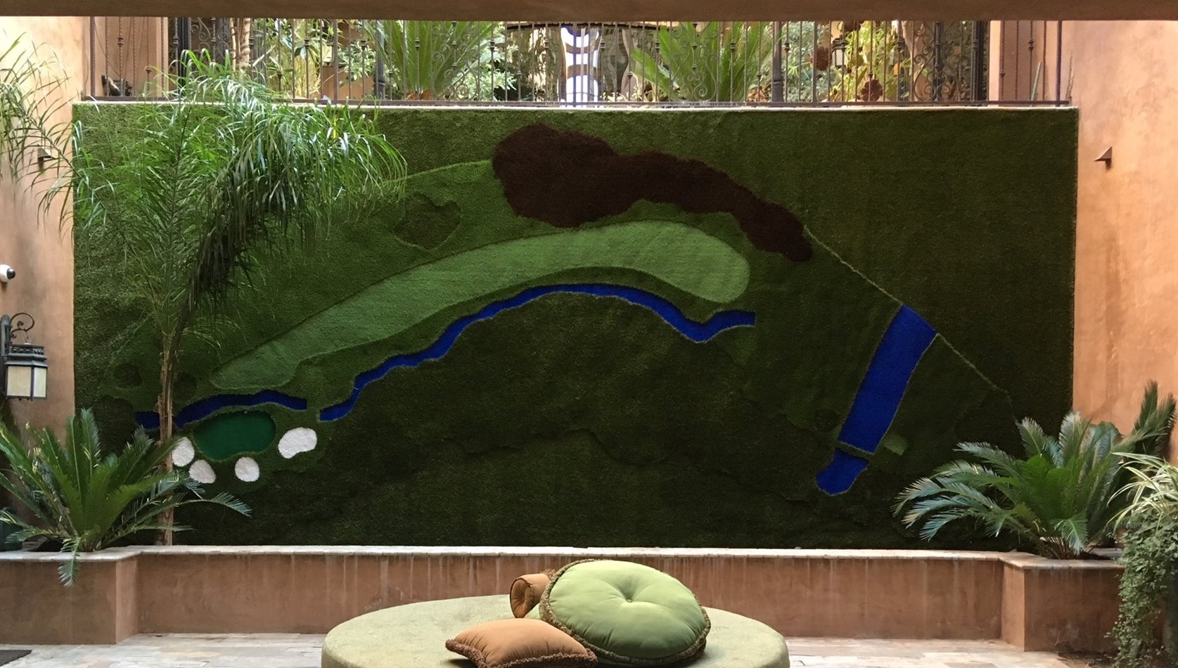 Custom artificial turf installation designed as a decorative wall mural featuring a 3D golf course landscape with green fairways, bunkers, and water features in a luxury courtyard setting.
